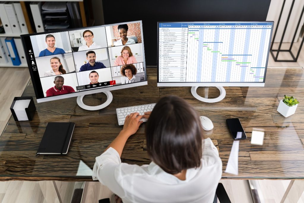 Una mujer delante de dos pantallas realizando un focus group online con un grupo de compañeros.